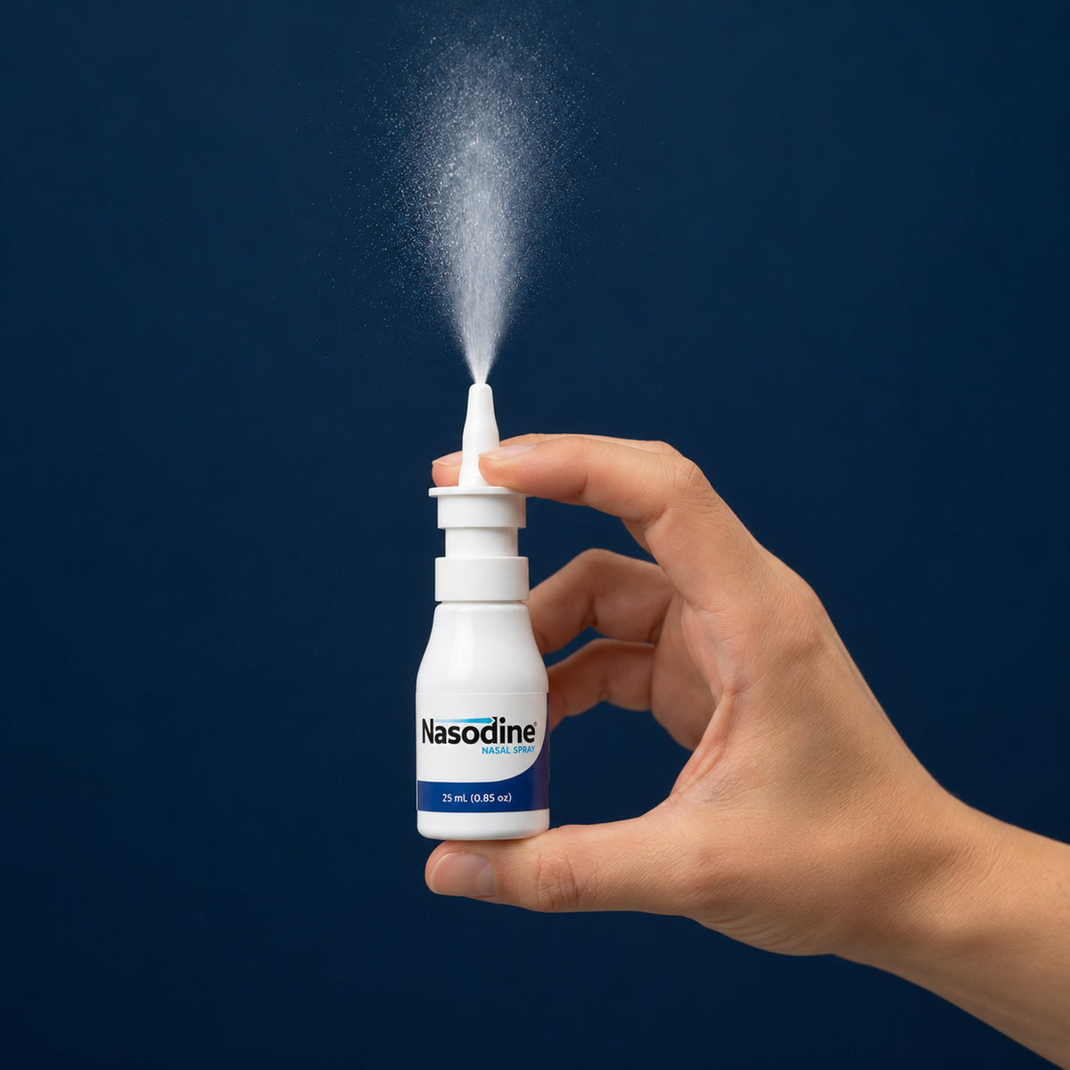 Hand pressing a Nasodine nasal spray bottle, releasing a fine mist